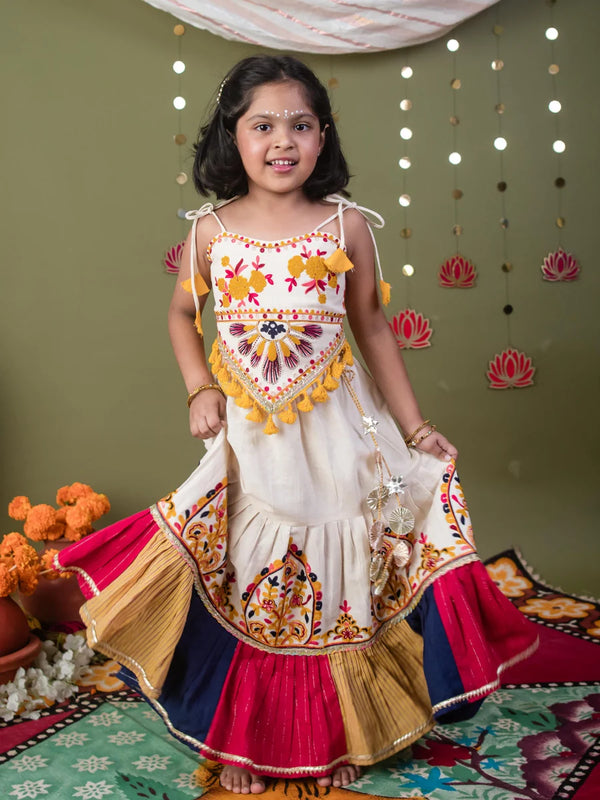 Young girl in a traditional outfit with colorful patterns and decorations, standing against a decorated wall.