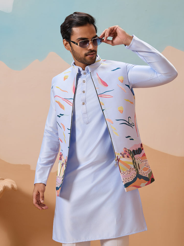 Man wearing a light blue kurta with a colorful jacket against a desert landscape.