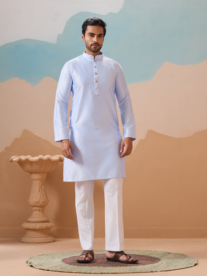 Man wearing a light blue kurta with white pants in a desert-themed setting