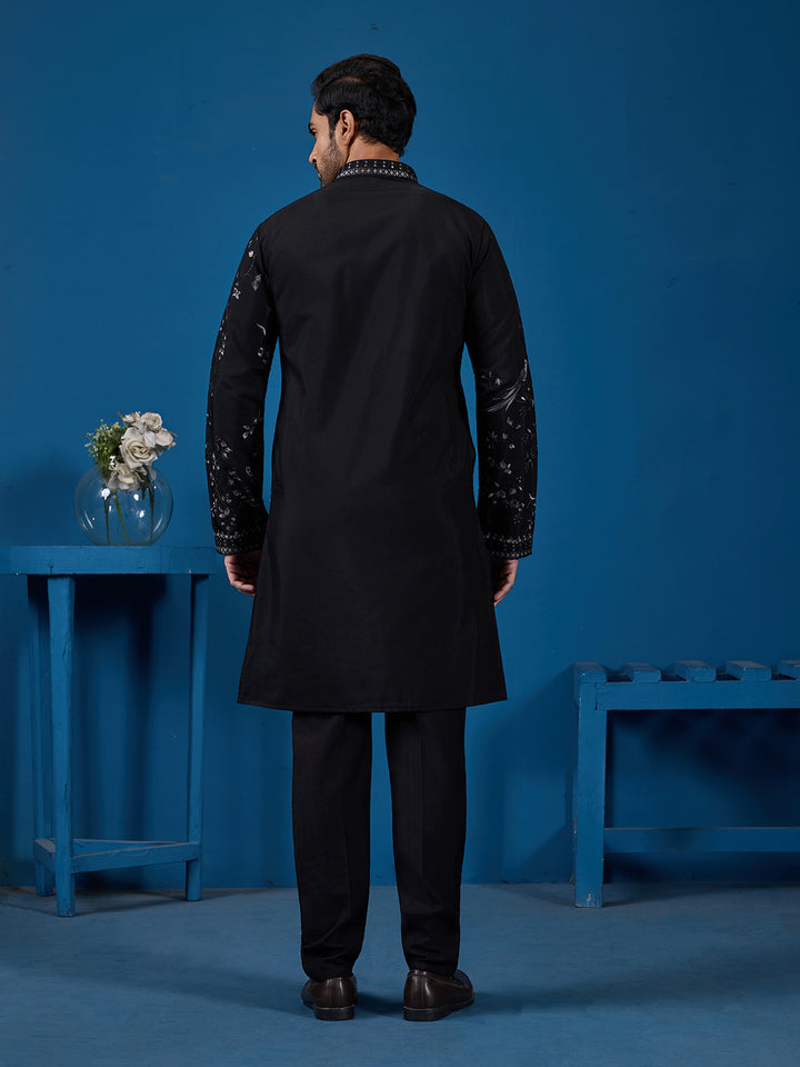 Man wearing a black kurta with embroidery standing against a blue background