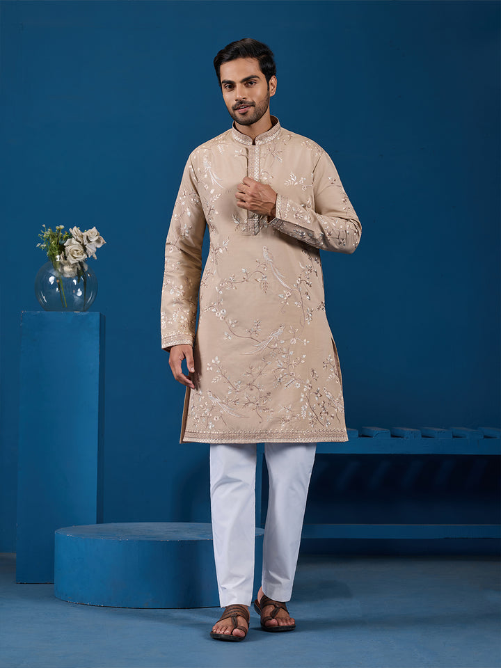 Man wearing a beige embroidered kurta with white pants against a blue background