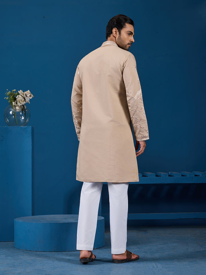 Man wearing a beige kurta with white pants against a blue background