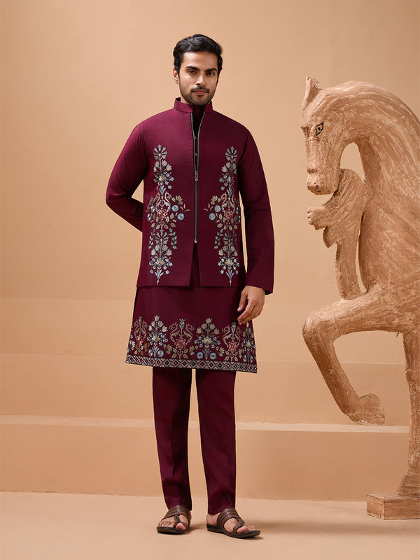 Man wearing a maroon embroidered traditional outfit standing next to a wooden horse sculpture on a beige background