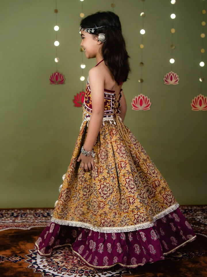 Young girl in a traditional outfit with a patterned dress against a green wall with decorative lights.