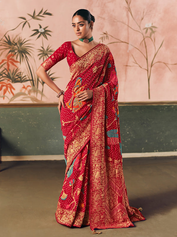 Woman wearing a red saree with intricate patterns against a decorative wall.