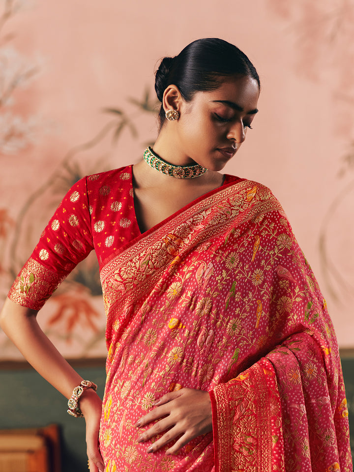 Woman wearing a red and pink saree with intricate patterns against a pink background
