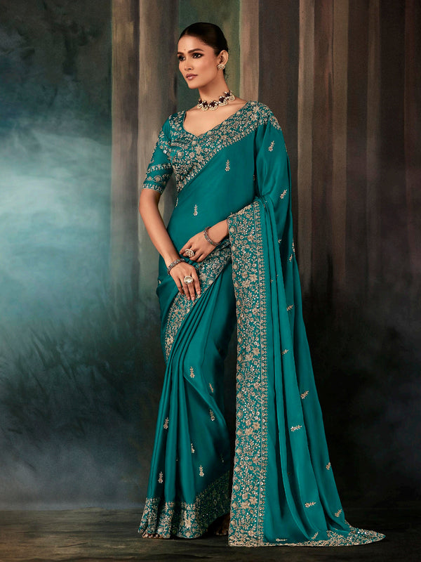 Woman wearing a teal saree with intricate patterns against a dark background