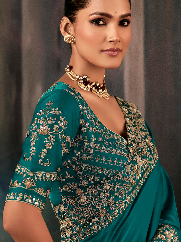 Woman wearing a teal saree with gold embroidery against a neutral background