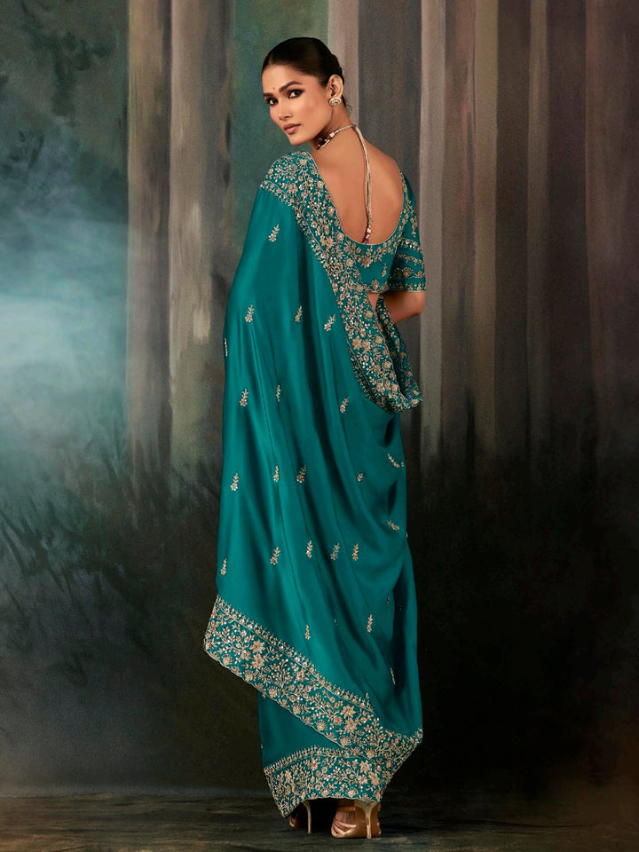 Woman wearing a teal saree with intricate patterns against a dark background