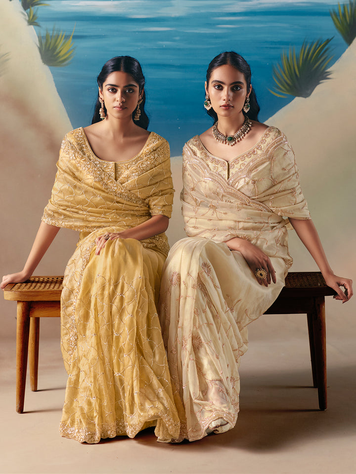 Two women in traditional embroidered sarees sitting on a bench with a scenic background.