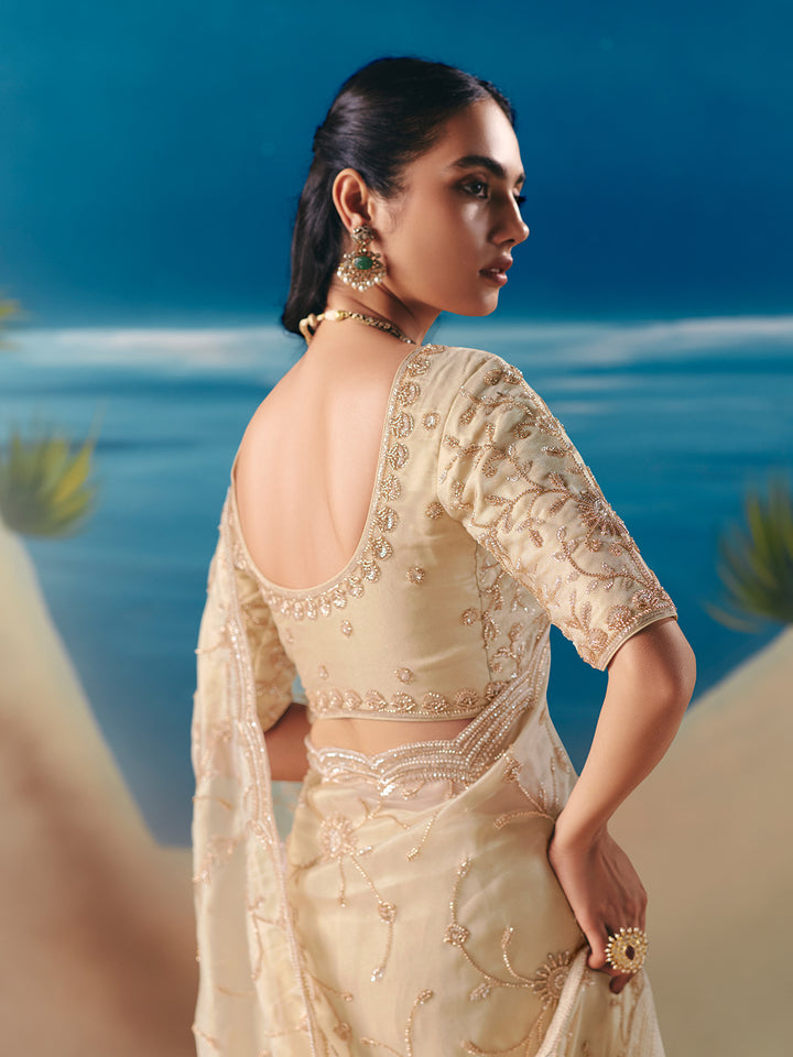Woman in a cream embroidered saree standing by the ocean