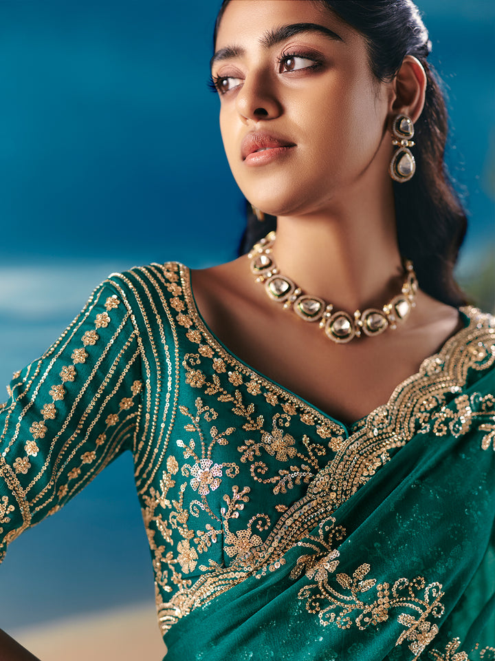 Woman wearing a green saree with gold embroidery and jewelry against a blue background