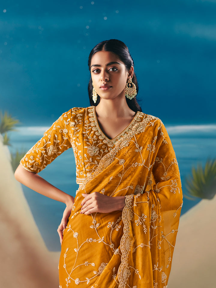 Woman in a yellow saree with gold embroidery against a blue ocean background