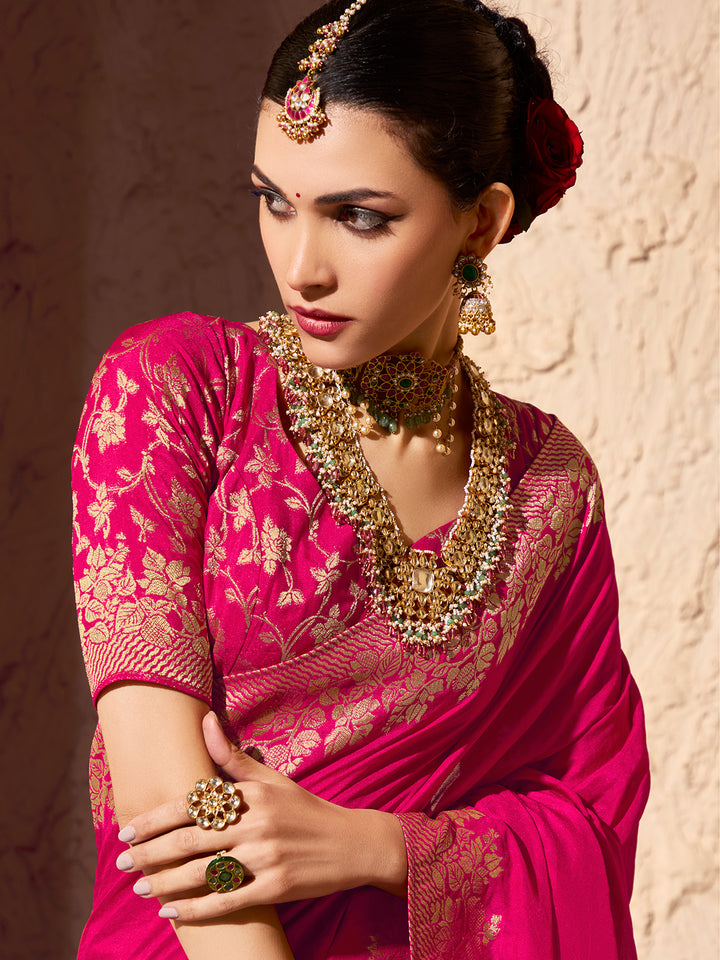 Woman in a pink saree with gold jewelry against a neutral background
