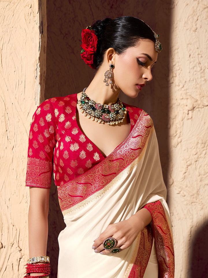 Woman wearing a red and white saree with jewelry against a textured wall.