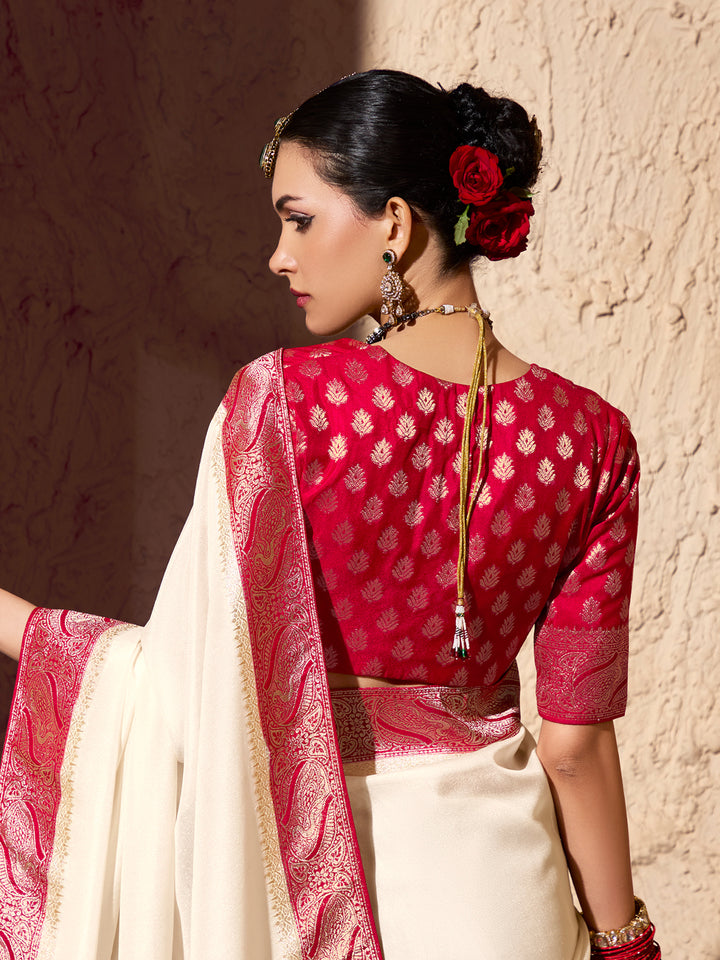 Woman wearing a red and white saree with a floral hair accessory against a textured wall.