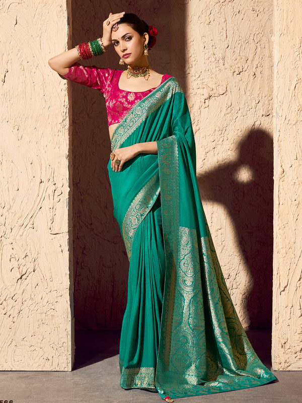 Woman wearing a teal saree with a pink blouse against a textured wall.