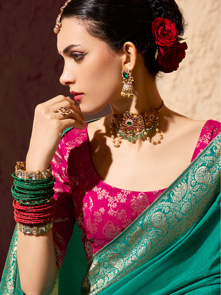 Woman in a pink and green saree with jewelry and floral hair accessory.