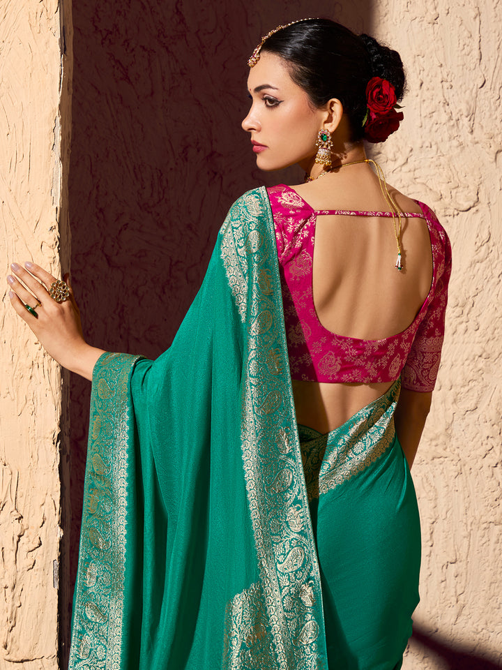 Woman wearing a green saree with a pink blouse against a textured wall.