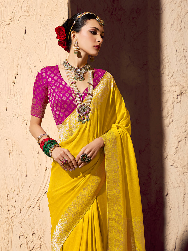 Woman in a yellow saree with a pink blouse against a textured wall.