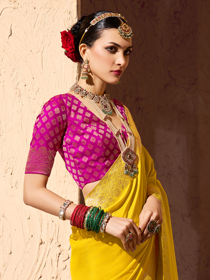 Woman in traditional Indian attire with a pink blouse and yellow saree, standing against a textured wall.