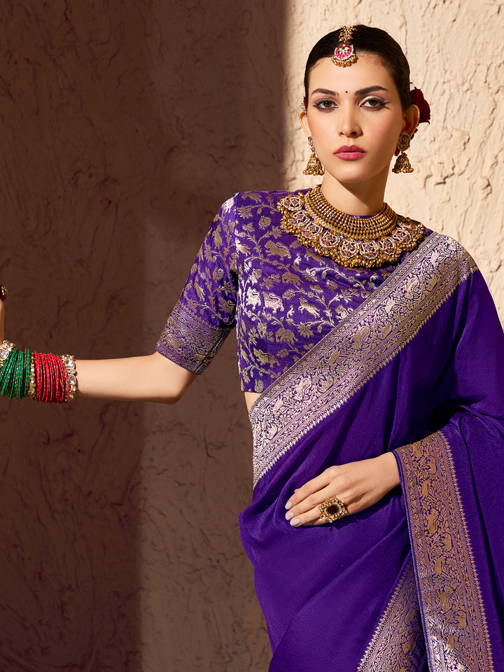 Woman wearing a traditional purple saree with gold embroidery against a textured wall.