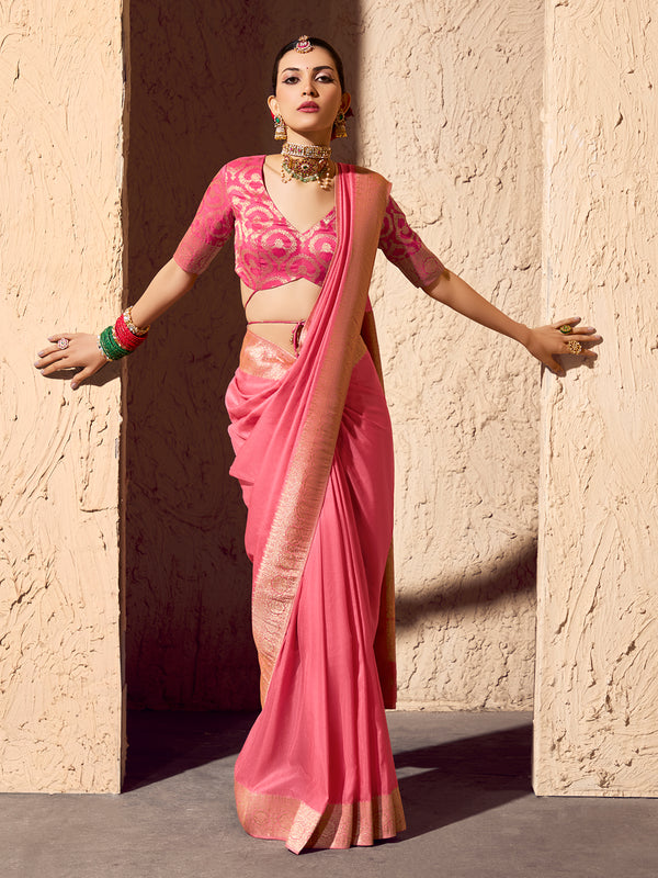 Woman in a pink saree standing against a textured wall.