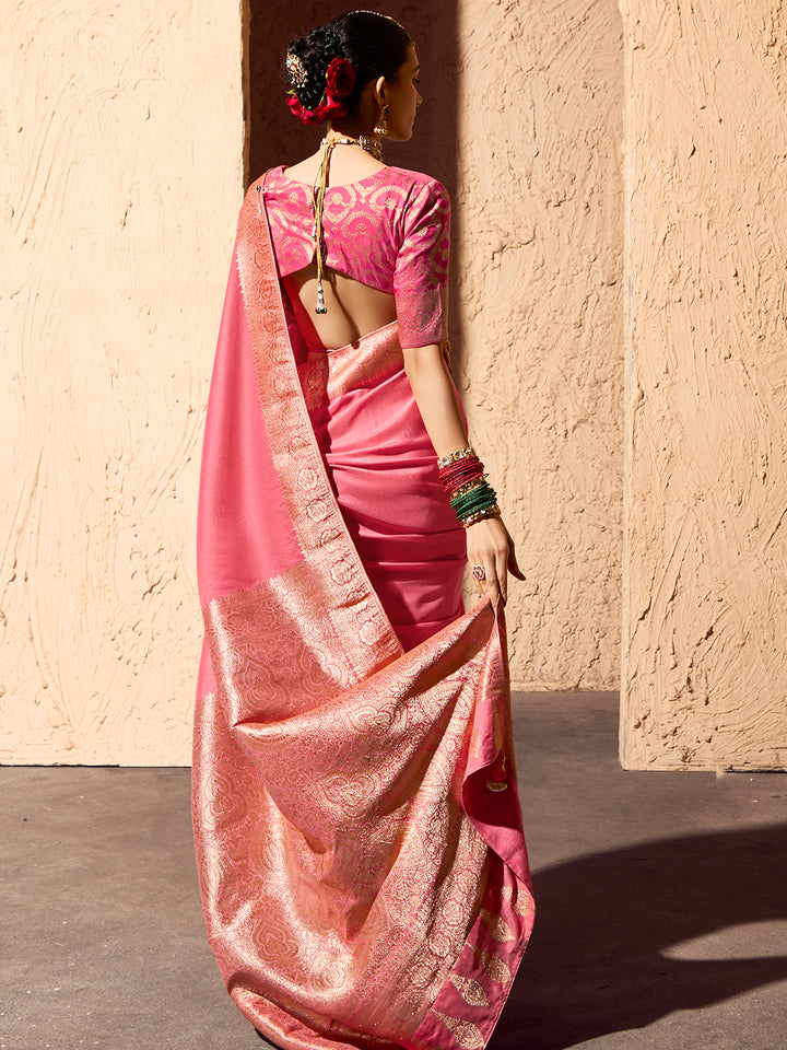 Woman in a pink saree standing against a beige wall.