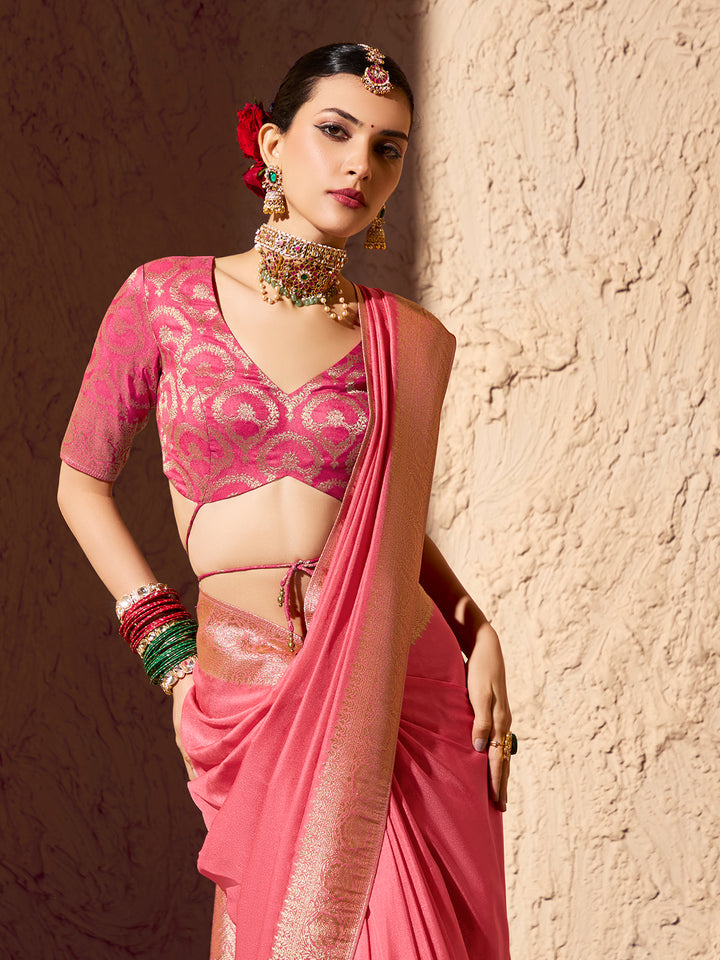 Woman in a pink saree with jewelry against a textured wall