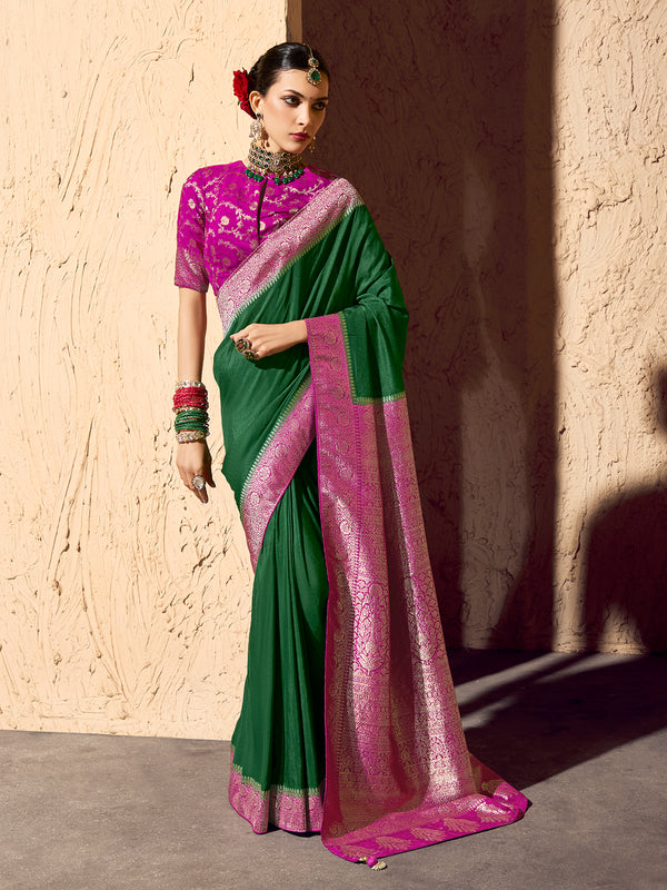 Woman wearing a green and pink saree with a matching blouse against a beige wall.