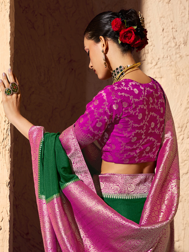 Woman wearing a vibrant pink and green saree against a textured wall.
