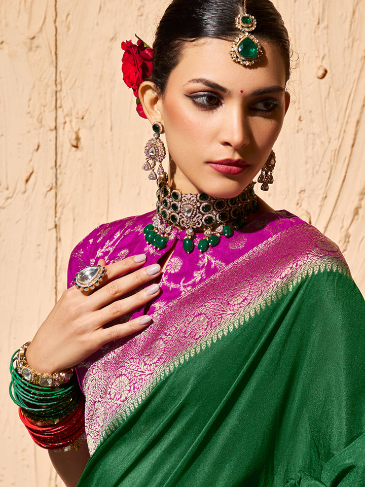 Woman wearing a green and pink saree with jewelry against a beige wall
