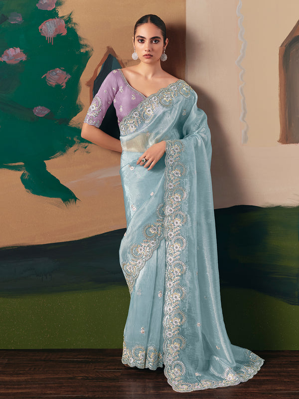 Woman wearing a light blue saree with white embroidery in a room with green and beige walls.