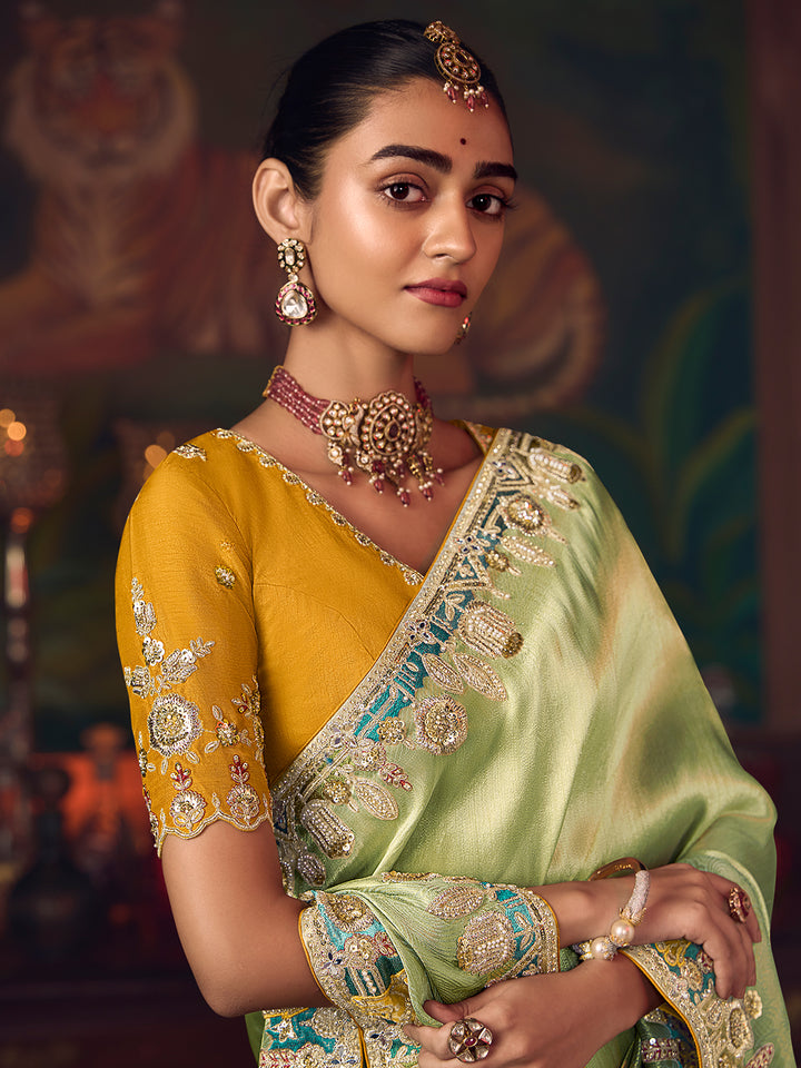 Woman wearing a traditional yellow and green saree with jewelry against a blurred background