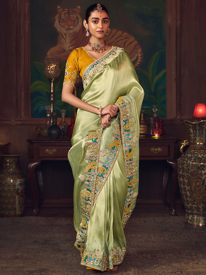 Woman in a light green saree with a yellow blouse in an ornate room.