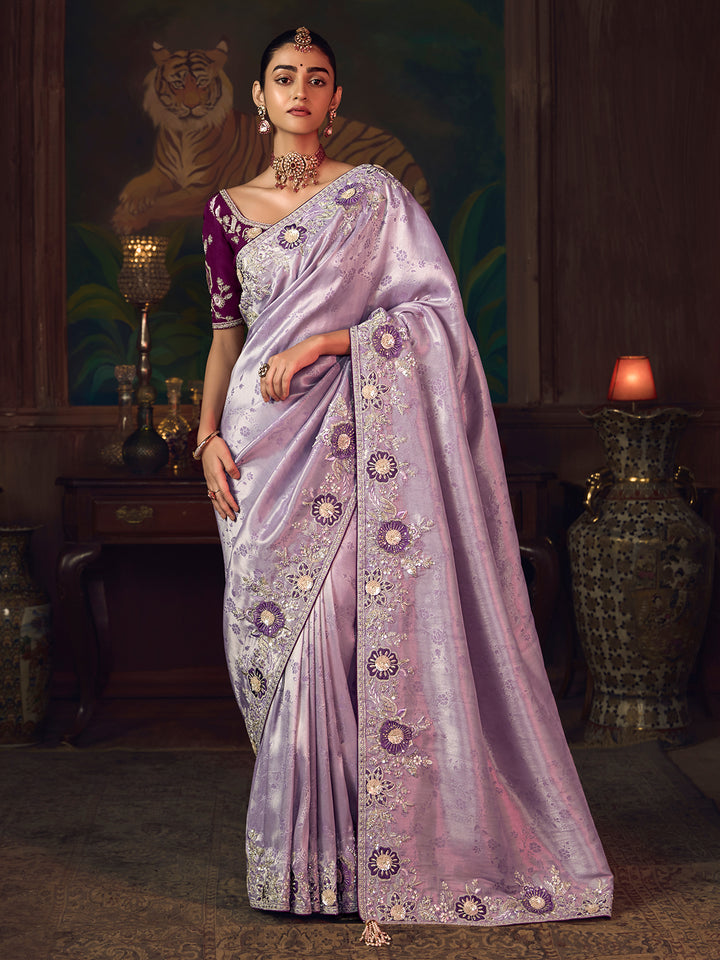 Woman in a lavender saree with intricate patterns in a decorative setting.