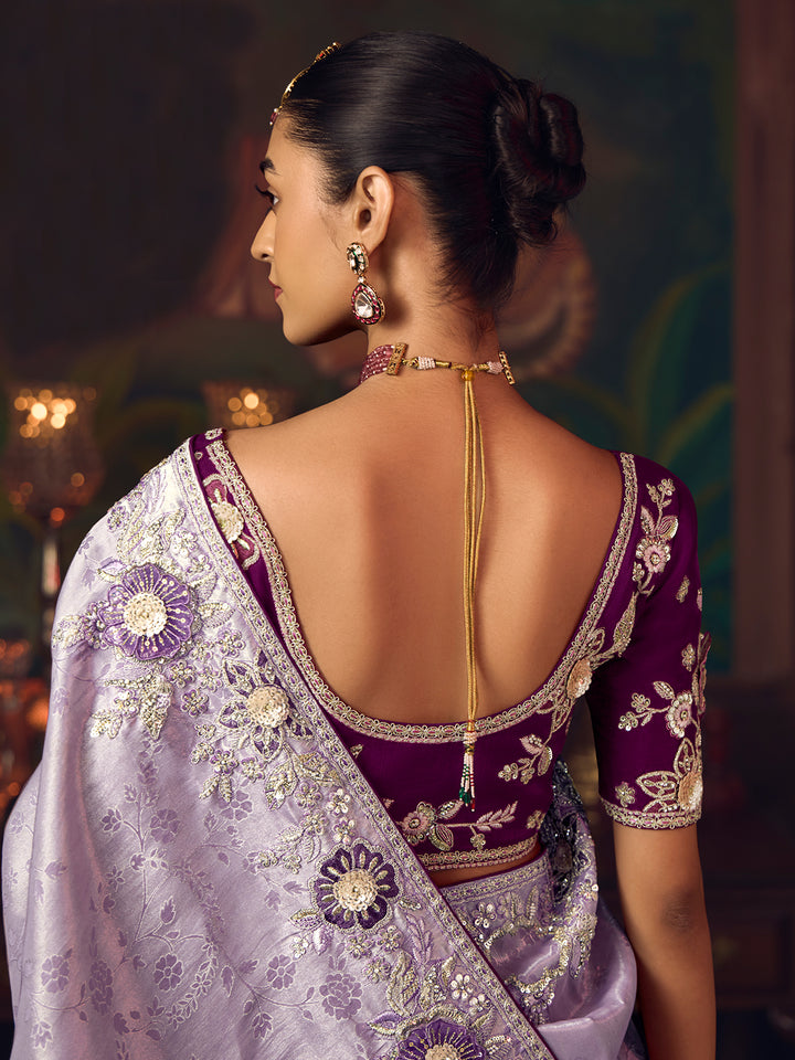 Woman wearing a traditional purple and white saree with intricate designs, back view.