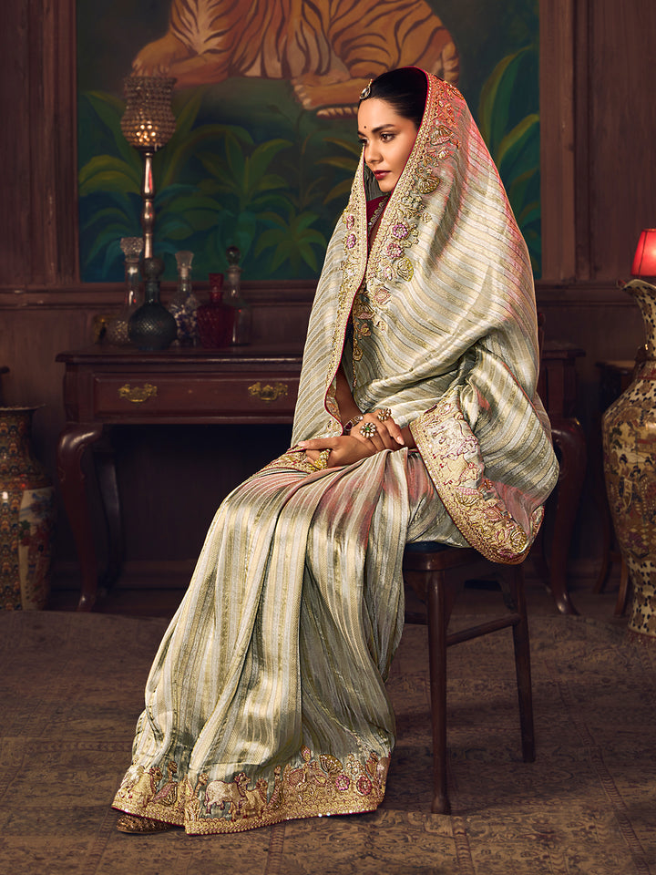 Woman in traditional embroidered saree sitting on a chair in an indoor setting.