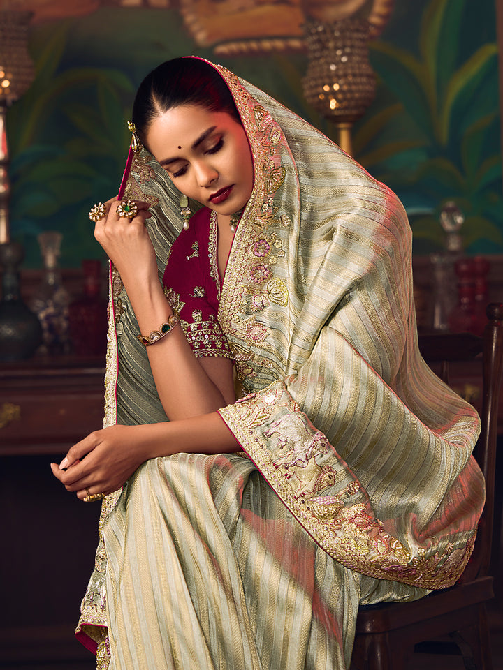Woman in a traditional saree with intricate patterns, sitting in a decorated room.