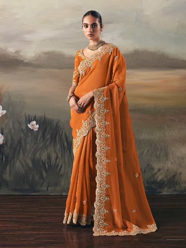 Woman in an orange saree with gold embroidery against a scenic background