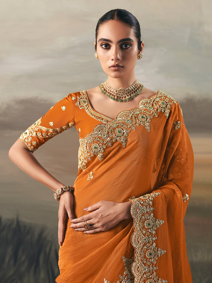 Woman wearing an orange saree with gold embroidery against a neutral background