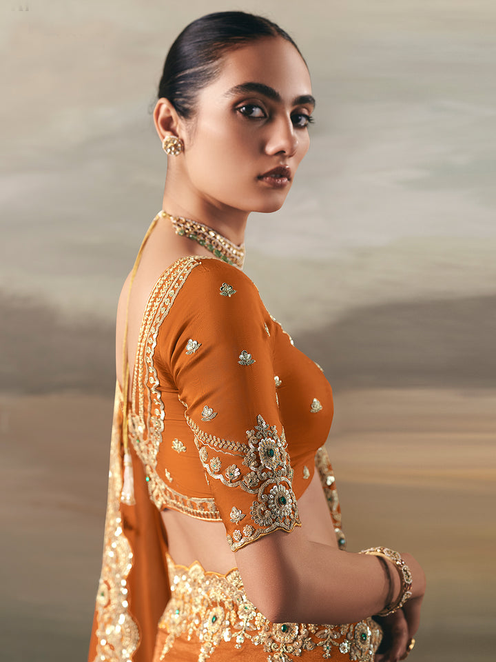 Woman wearing an orange traditional outfit with gold embroidery against a neutral background
