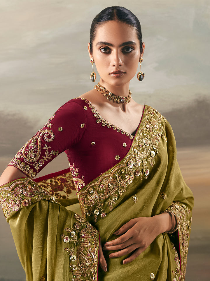 Woman wearing a traditional green and maroon saree with intricate designs against a neutral background