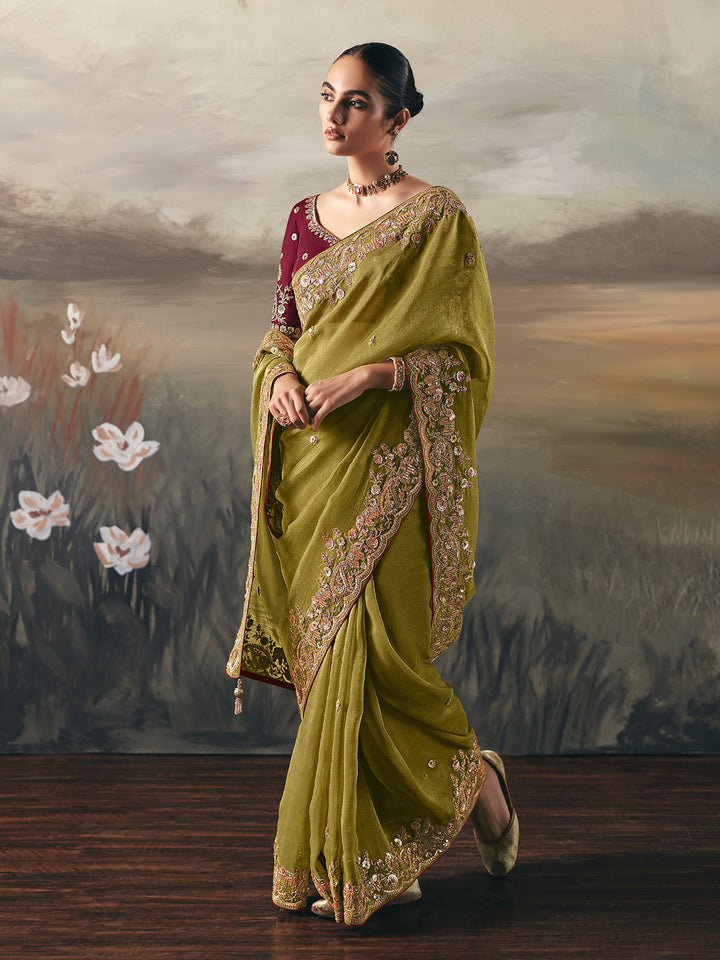 Woman in a green saree with gold embroidery standing against a scenic background