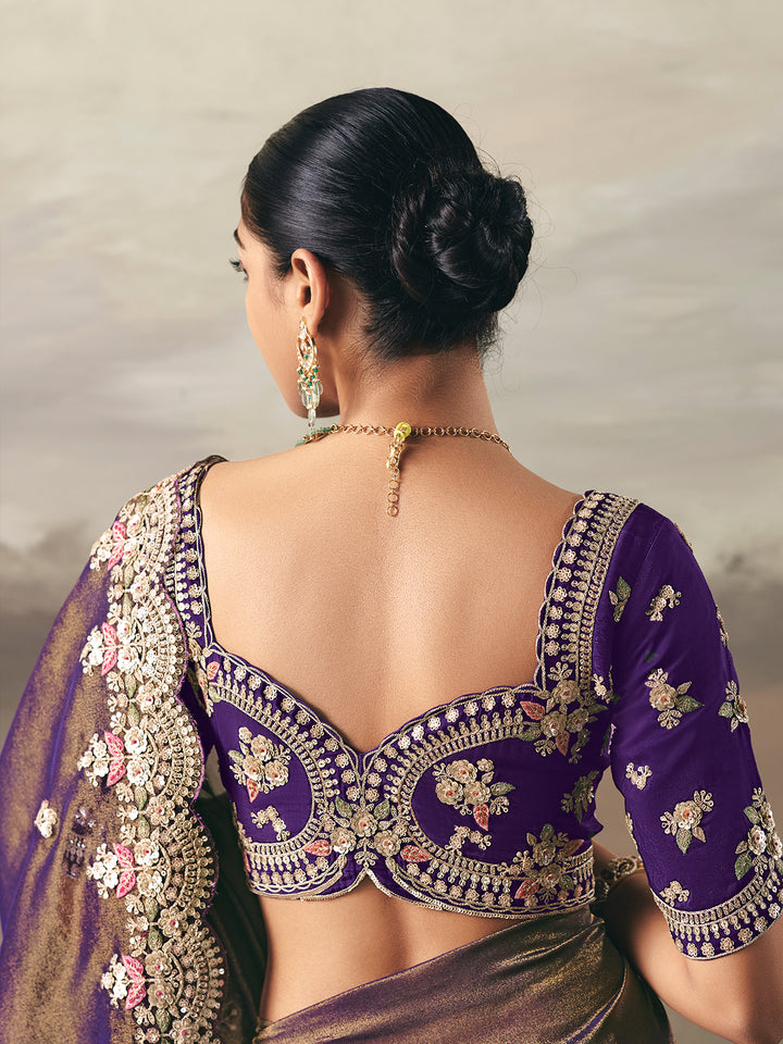Woman wearing a purple saree with intricate gold embroidery against a neutral background