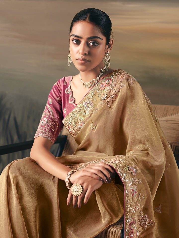 Woman in a traditional beige saree with pink blouse, sitting against a neutral background