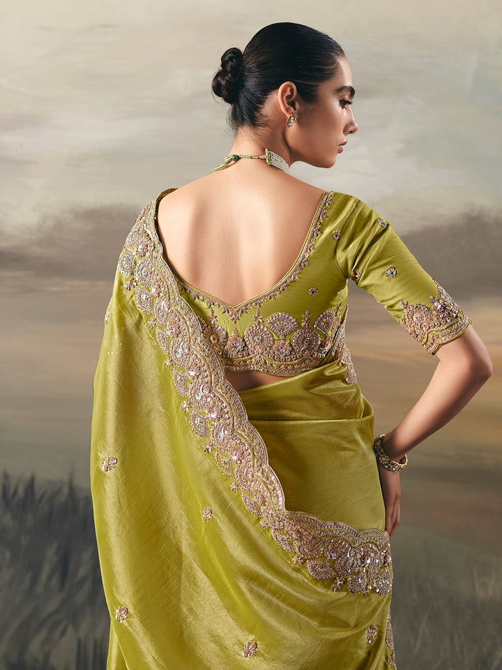Woman wearing a light green saree with intricate gold embroidery against a natural background