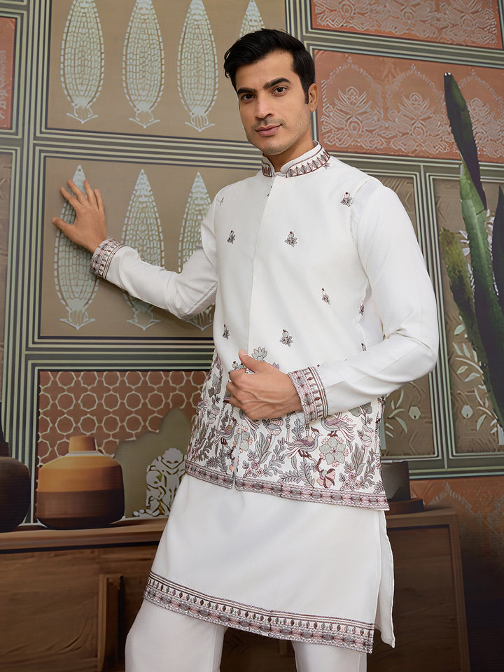 Man wearing a traditional white embroidered outfit in a decorative room.