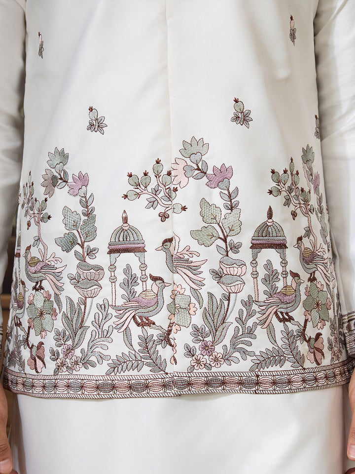 Close-up of a white garment with intricate floral and bird embroidery.