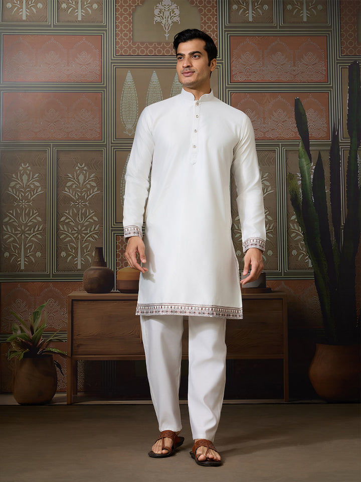 Man wearing a white kurta with embroidery in a decorated room.